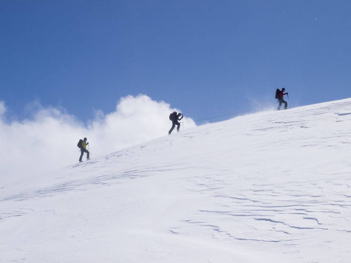 Three ski tourists walking to the summit - Powderaddicts