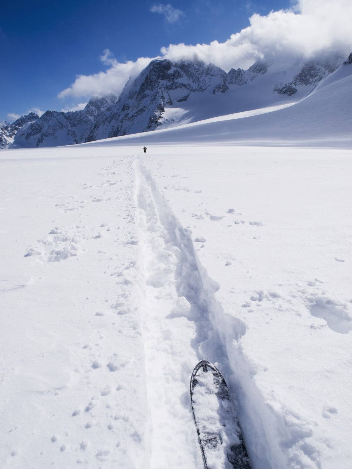 Two distant skiers ski touring across the Ottemma glacier, with skinning tracks - Powderaddicts
