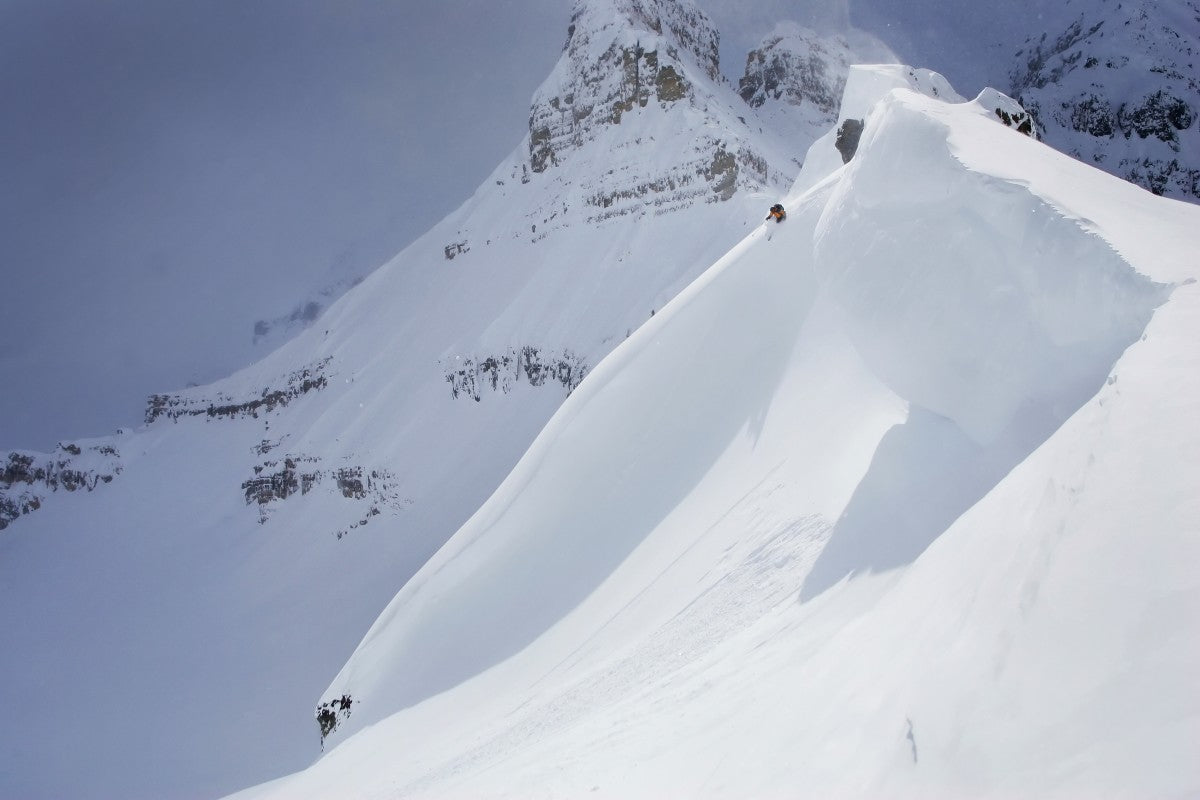 Skier On Crest Of Big Drop, Dwarfed By Mountain; Canada, British Columbia, Icefall Lodge - Powderaddicts